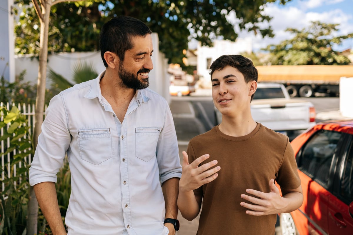 Teenage son speaks while his father listens attentively during an outdoor walk